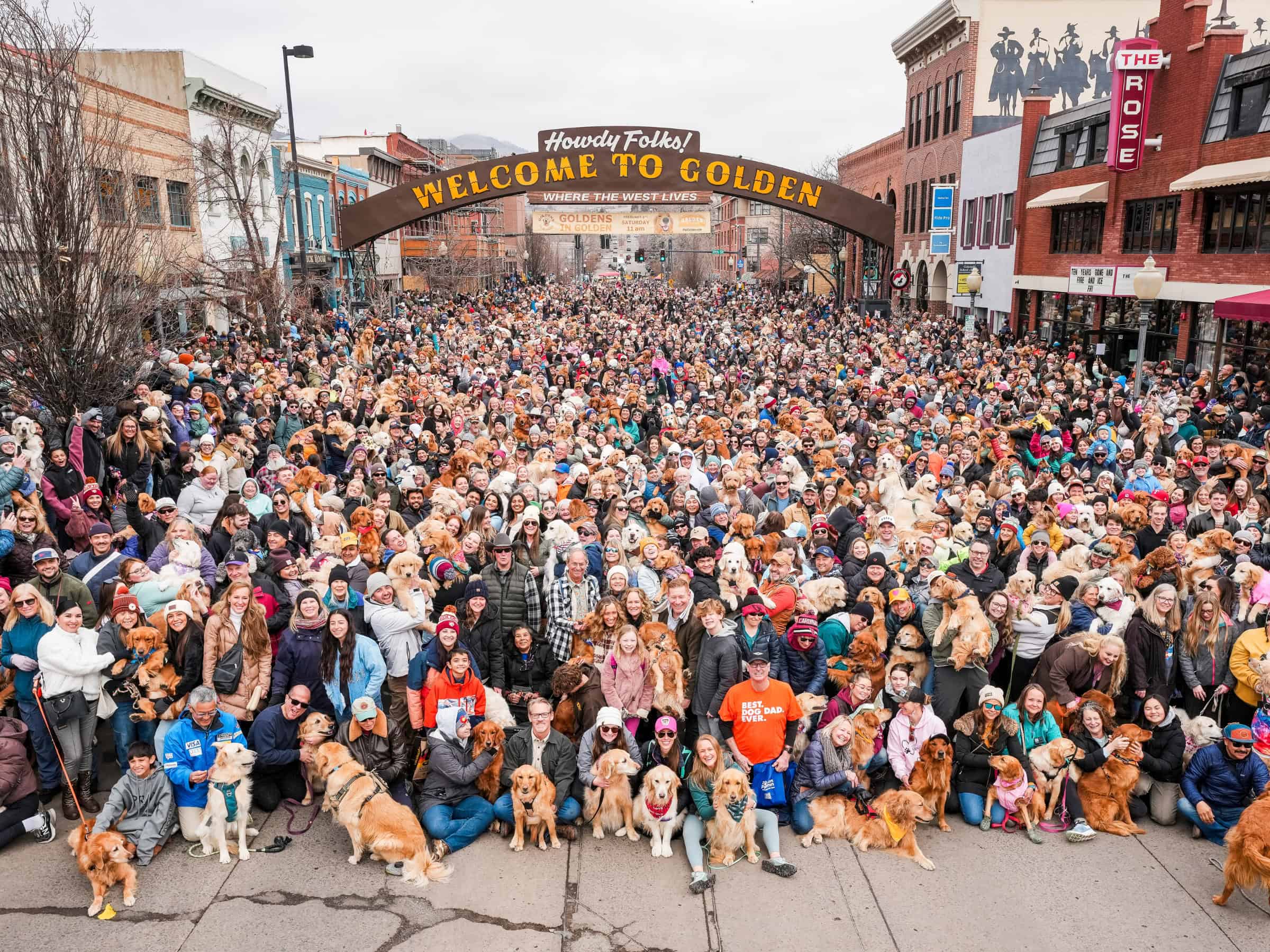 Thousands of Golden Retrievers and their owners gathered under the Welcome to Golden sign in downtown Golden, Colorado during the Goldens in Golden 2025 event.