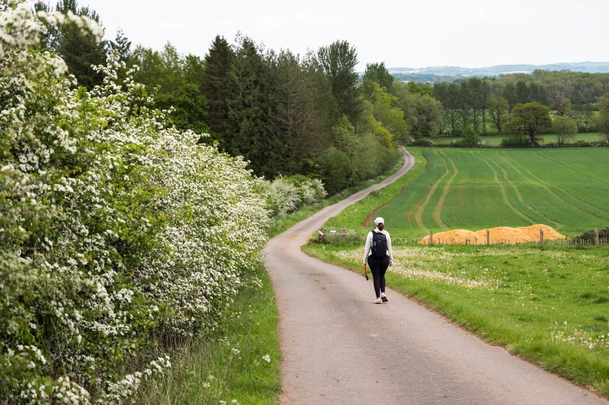 Woman walking a narrow country road in the Cotswolds countryside England