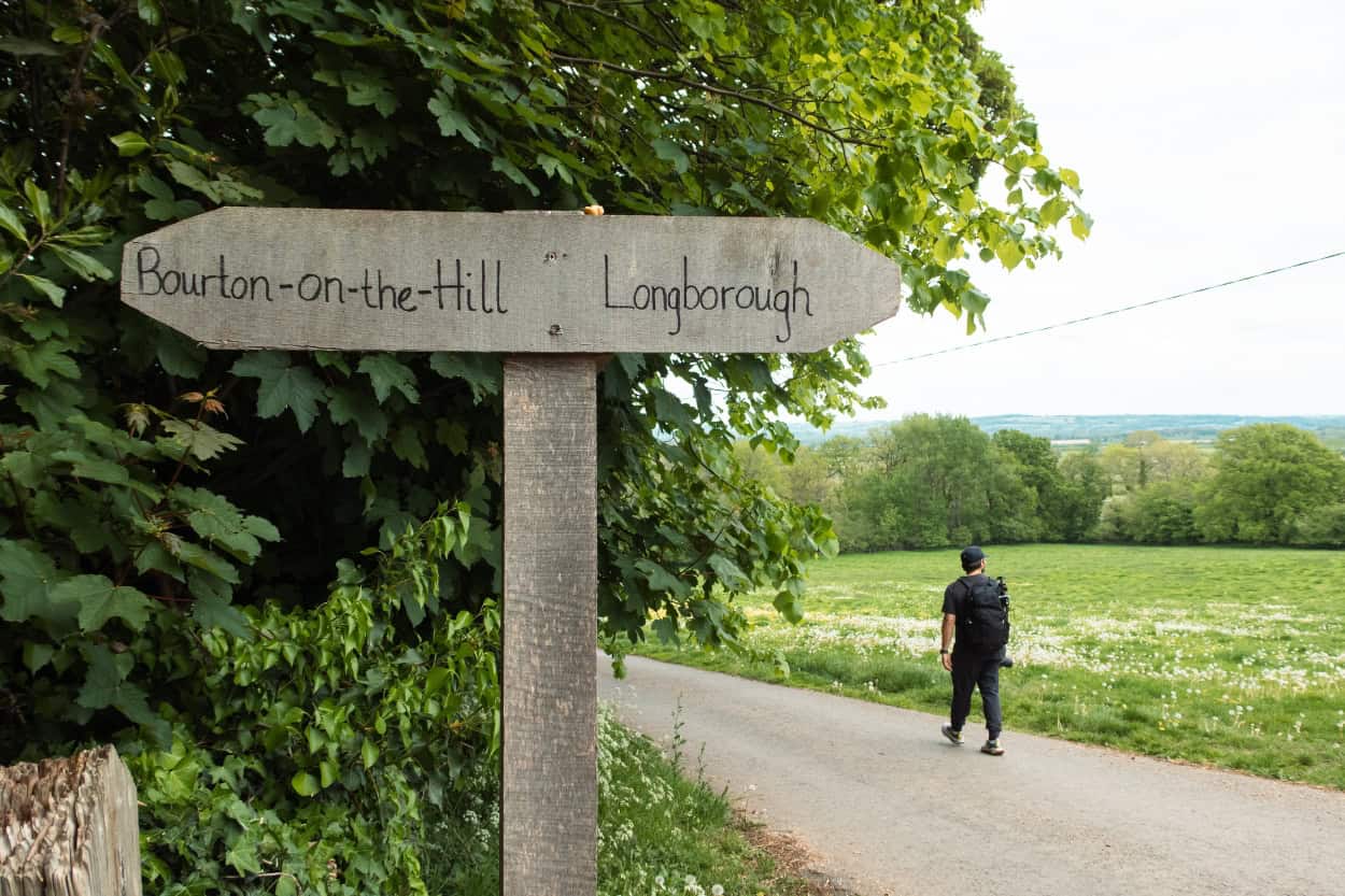 Trail signpost near Longborough in the Cotswolds with Joey walking in the background. Macs Adventure Review.
