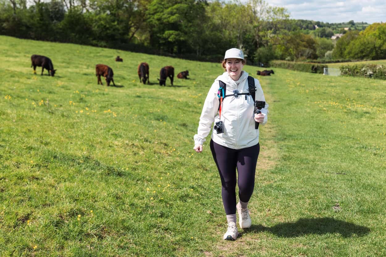 Katie walking through a green field with a big smile during her Macs Adventure trip in England
