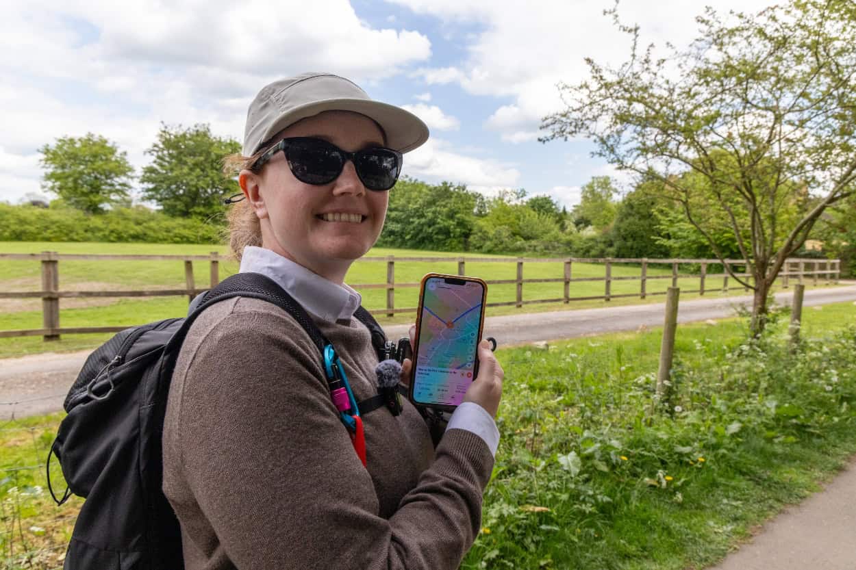 Katie holding up the Macs Adventure app while walking through the Cotswolds in England