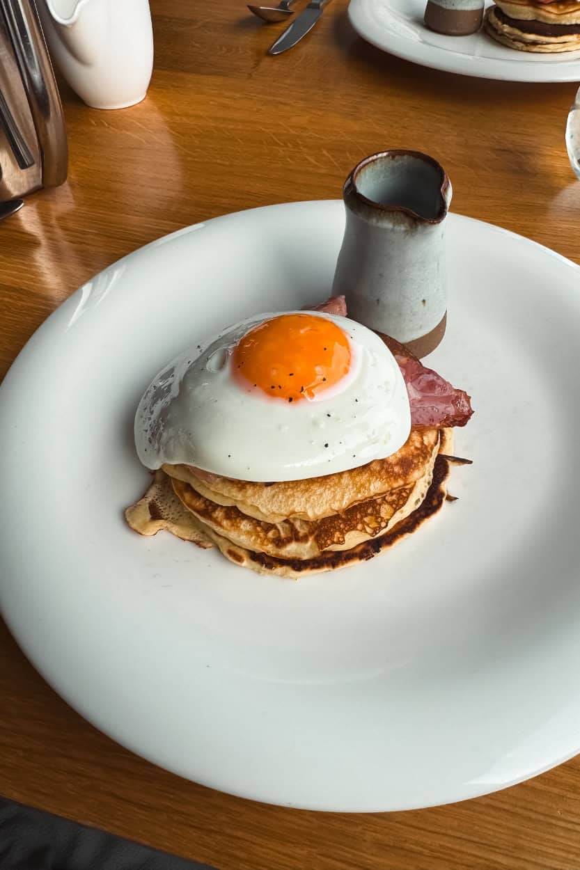 Stack of pancakes topped with a fried egg and bacon at Boskerris Hotel in St. Ives