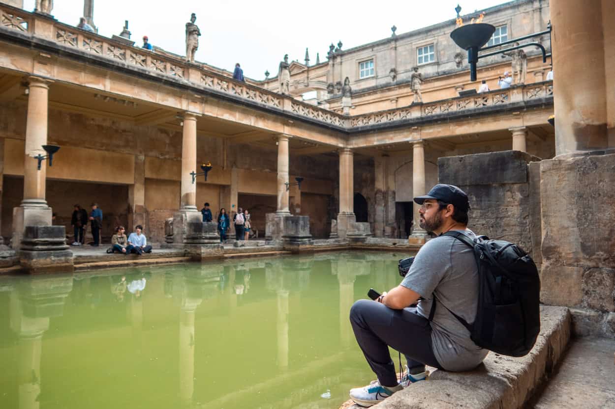 Joey sitting beside the green thermal water of the Roman Baths in Bath, England