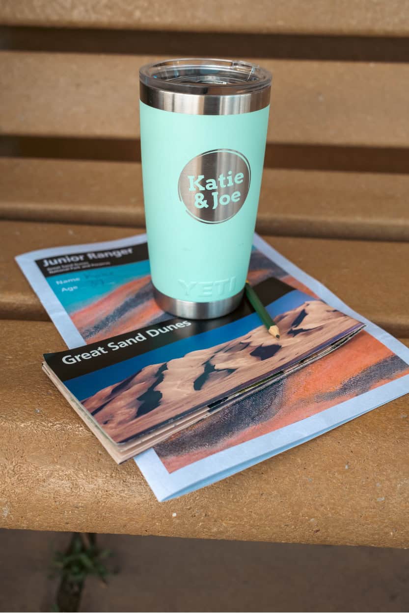 Katie and Joe coffee tumbler on a map and Junior Ranger booklet at Great Sand Dunes National Park