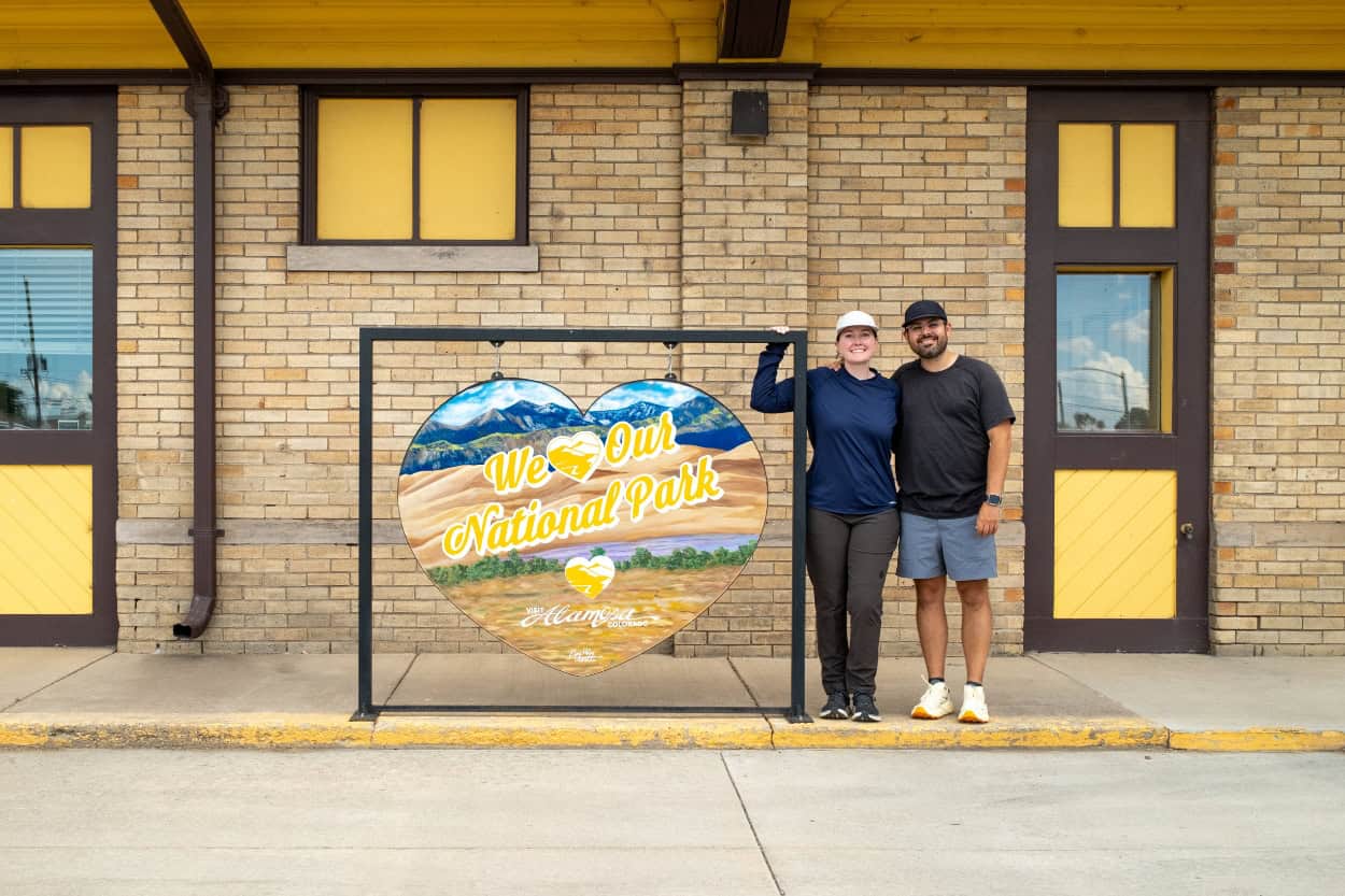 Couple standing in front of a "We Love Our National Park" sign at the Alamosa Visitor Center in Colorado