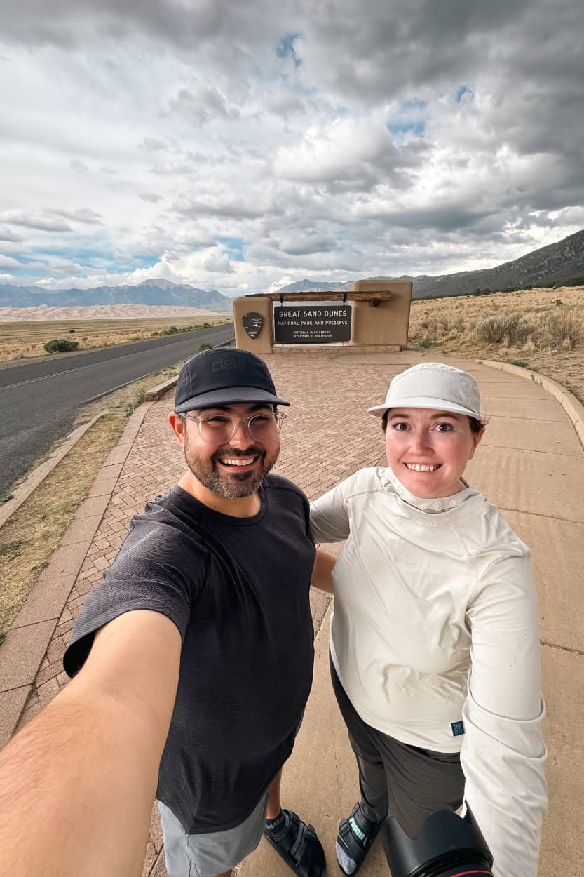 Couple standing in front of the Great Sand Dunes National Park entrance sign in Colorado